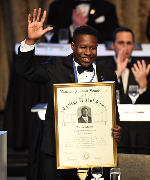 Former Georgia Southern star Adrian Peterson holding the certificate of the college hall of fame and waving