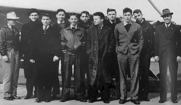 a shot from 1940 of 11 men standing in front of a small plane