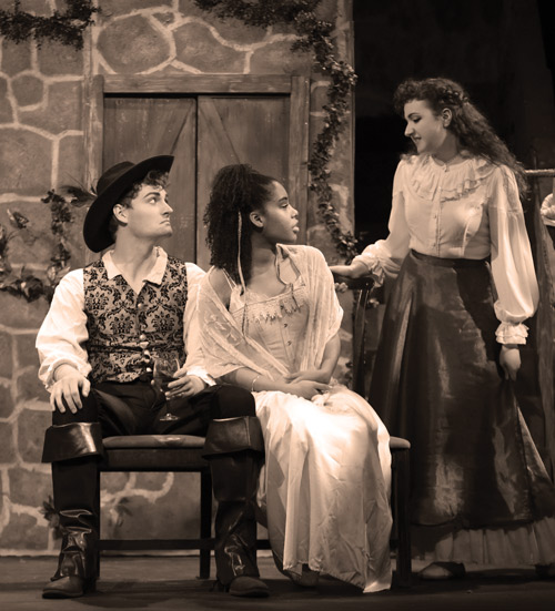 photo from 1937 showing a man in clothing like the three musketeers sitting next to a woman in a long flowing dress talking to a woman standing next to them