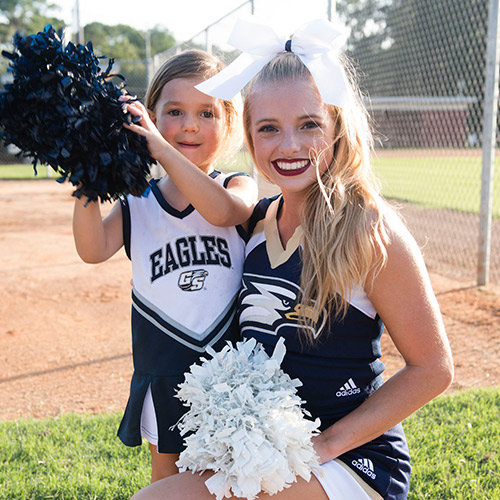 cheerleader posing with young girl holding pom poms