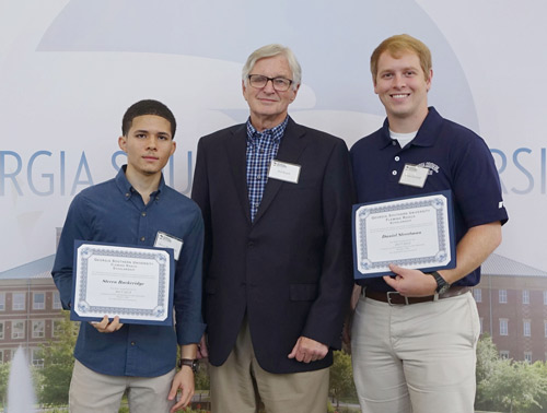 three men standing in front of a Georgia Southern backdrop two with scholarship certificates