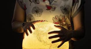 A student holds their hands over a glowing globe